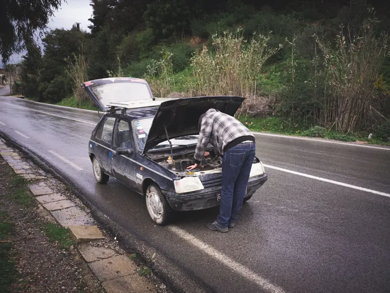 Vozač pod podignutom haubom auta na mokroj cesti